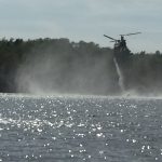 Heavy helicopter hovering over a lake and drawing water to drop on the fire.