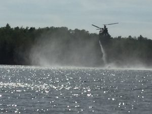 Heavy helicopter hovering over a lake and drawing water to drop on the fire.