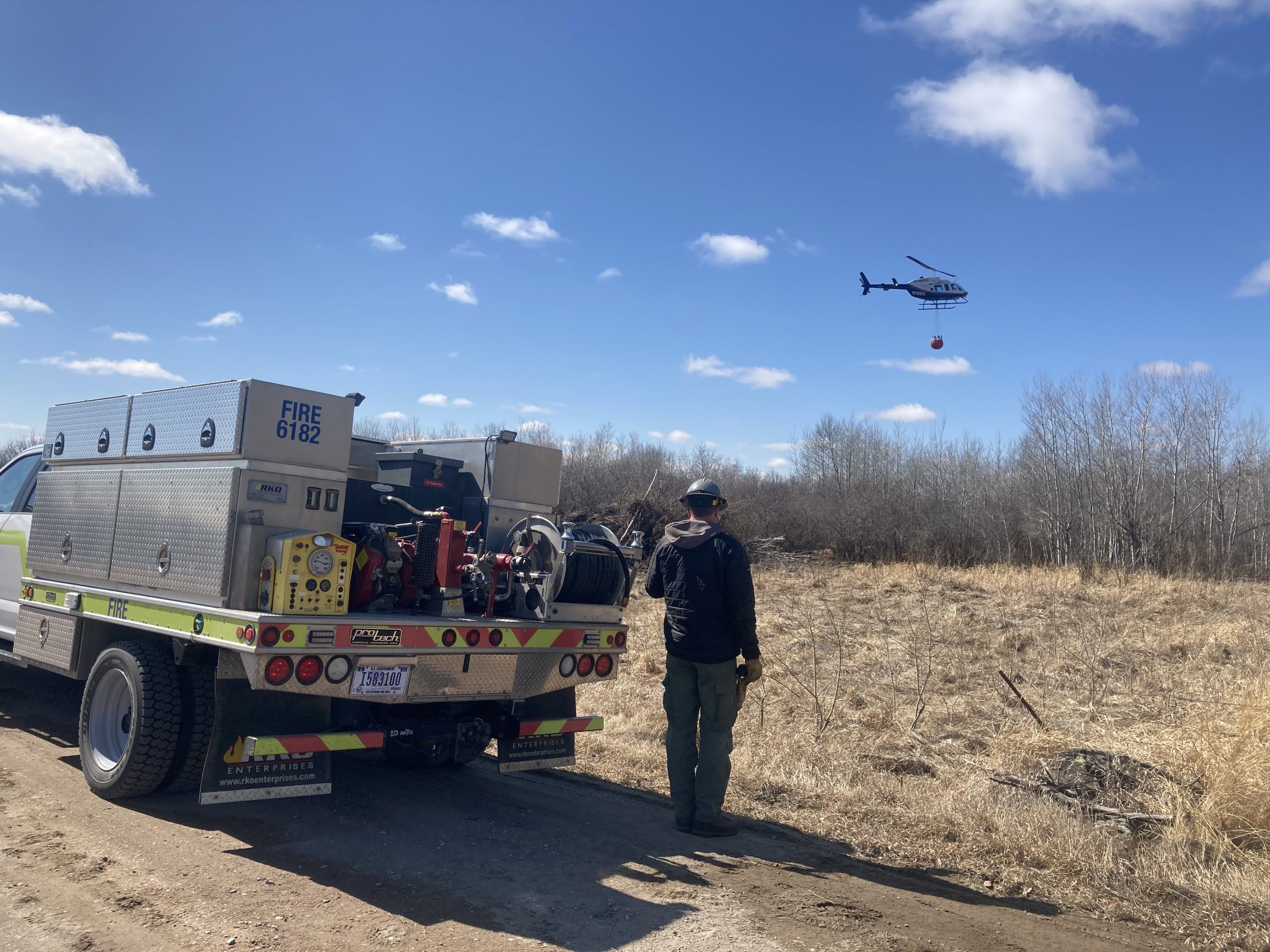 Firefighter next to engine faces helicopter with bucket
