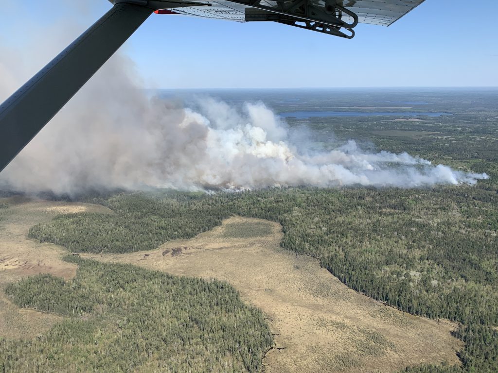 aerial view of land with smoke rising next to lake.