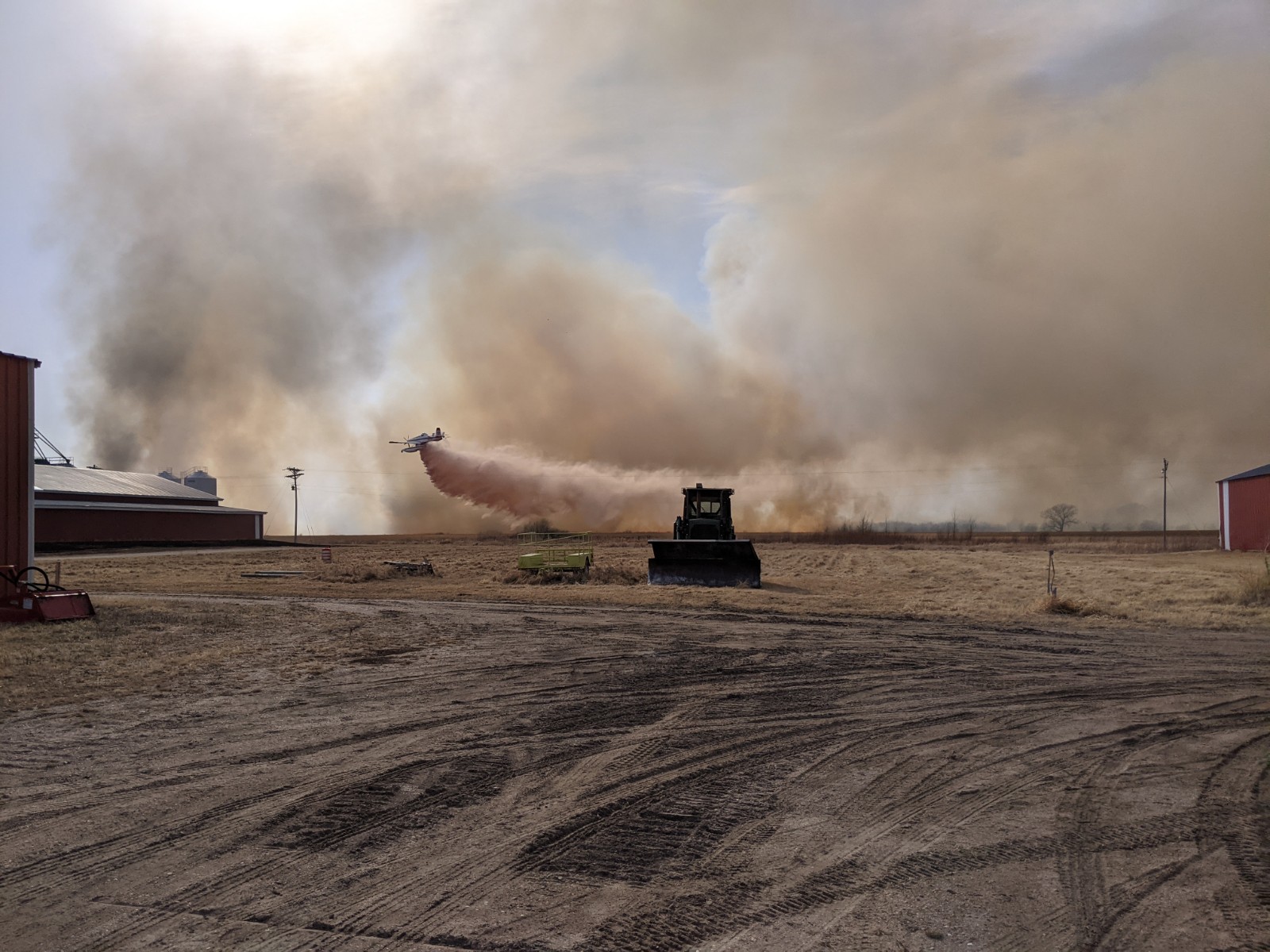 Aircraft drops water on smoky area next to farm equipment.