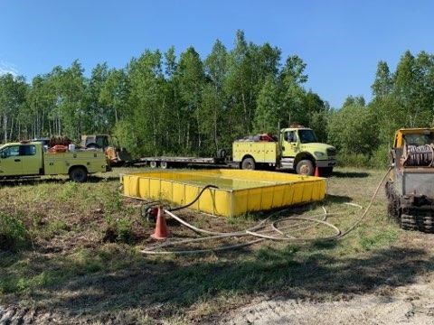 Yellow tank and yellow fire engines in front of trees.