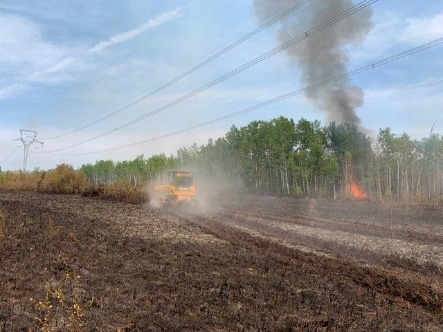 Tractor scraps dirt near powerlines, trees, and wildfire.