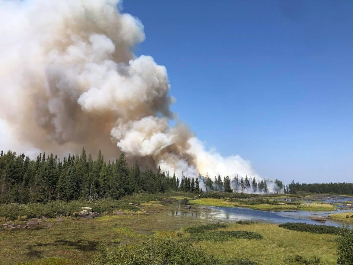 Wwhite smoke rises next to blue sky and green meadow.