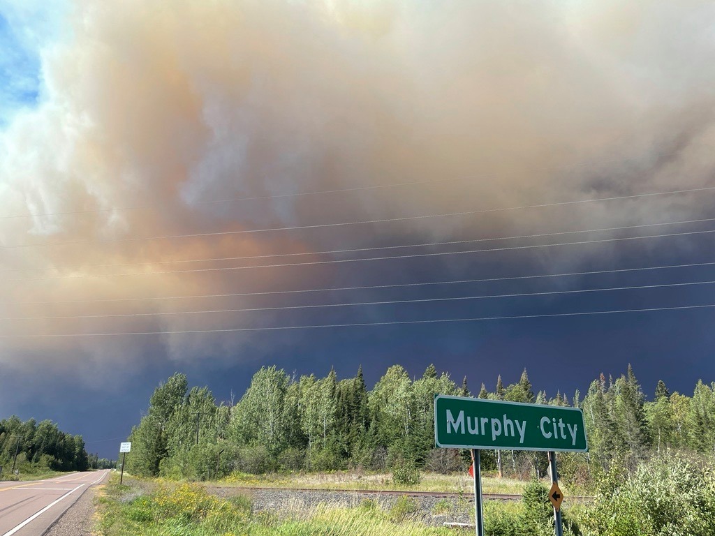 Dark smoke fills sky above highway and forest.
