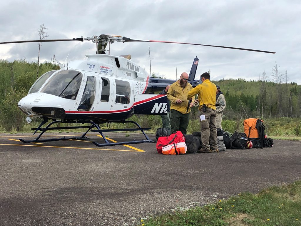 Helicopter and people in yellow shirts load backpacks.