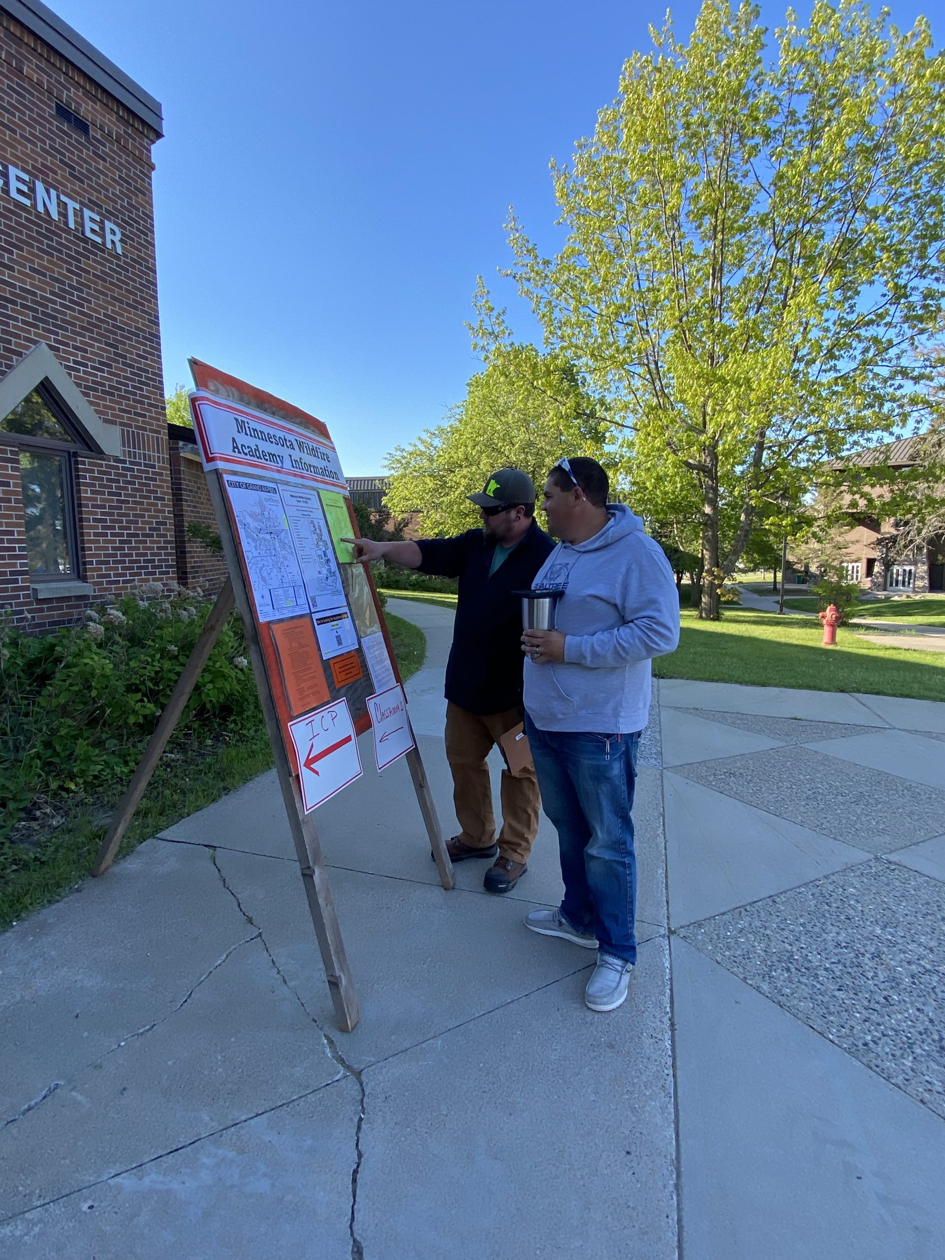 Two people look a wooden board with information signs and maps.