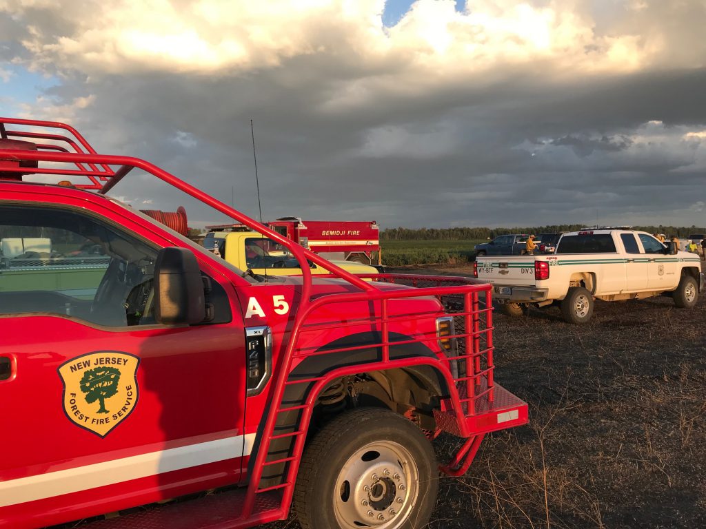 Red fire truck sits in front of two trucks in the background in an open field.