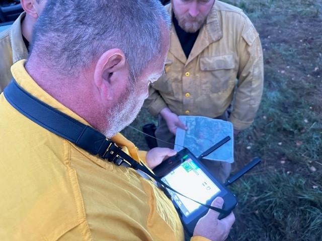 Image looking down on three men looking at an electronic screen. 