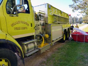 A large yellow fire engine fills up a red portable tank with water.