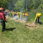 A group of people wearing yellow shirts hold firing devices to the ground in a training session.