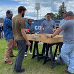 A group of five people stand around a wood sand table box.