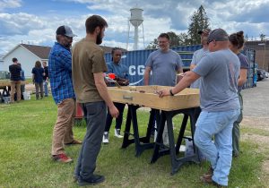 A group of five people stand around a wood sand table box.