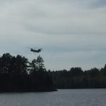 A helicopter hovering over the trees on the edge of Burntside Lake.