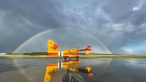 CL 415 EAF Aircraft sitting on runway on rainy evening with rainbow arcing over it in background