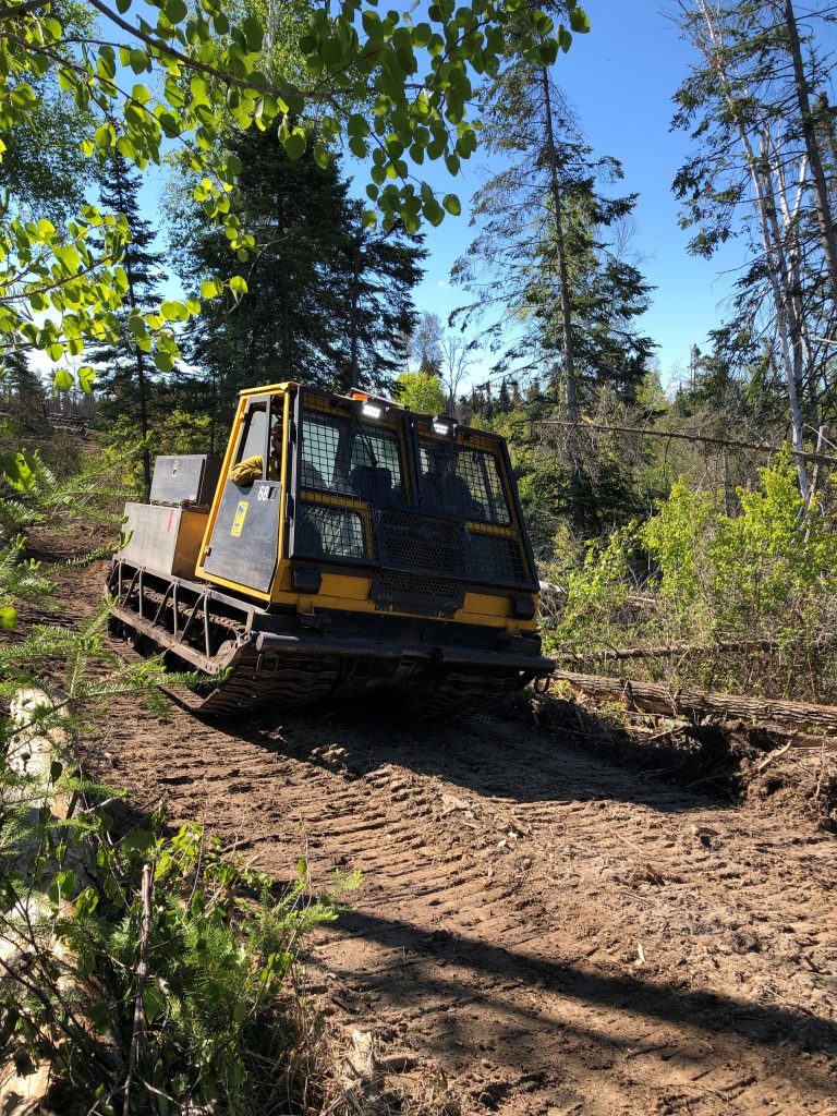 Tracked vehicle in on dirt path near trees.