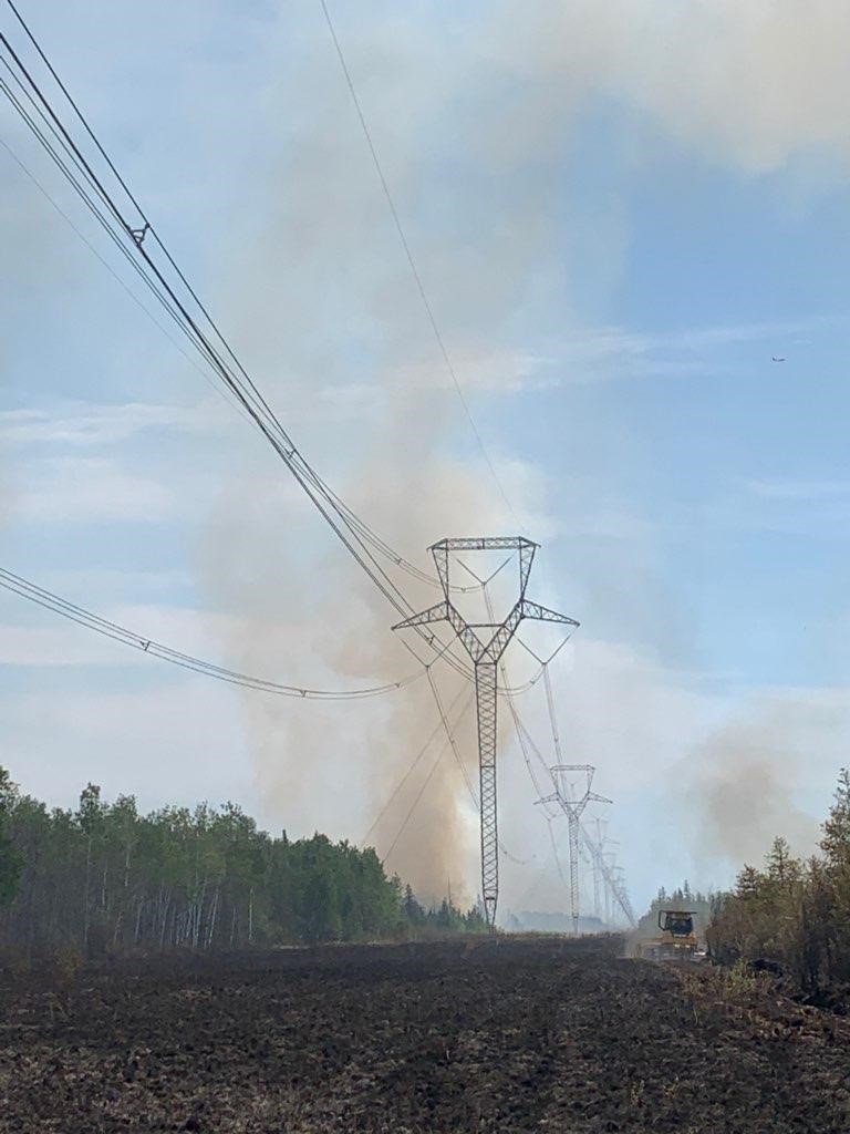 Smoke rises next to power with a tractor moving through dirt.