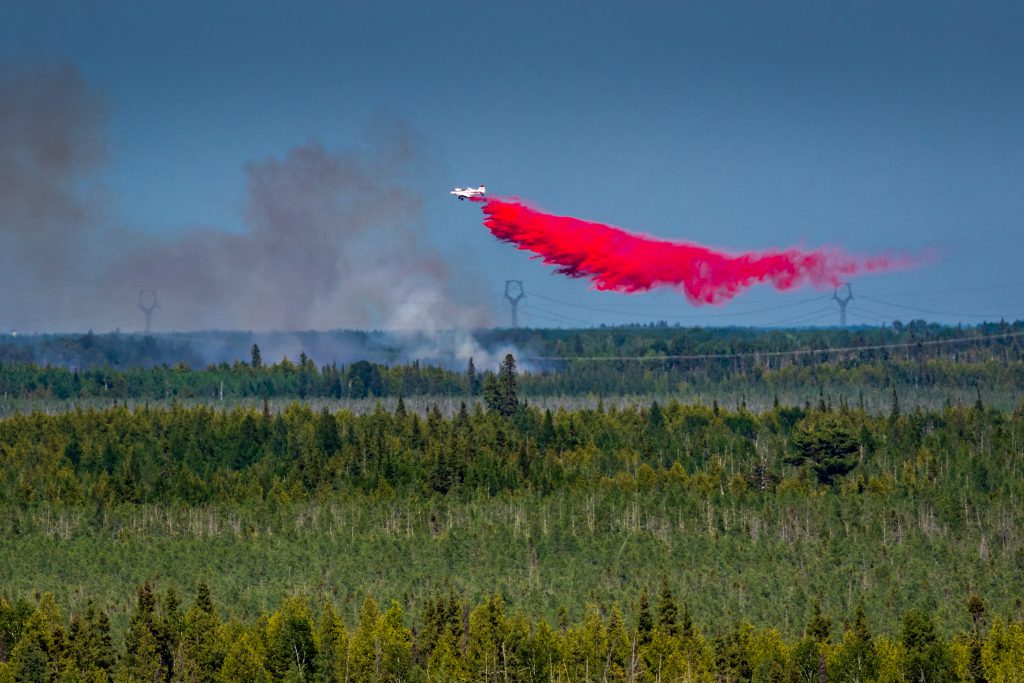 Aircraft dropping red retardant above trees.