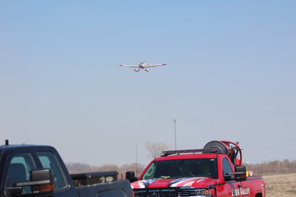 Low flying airplane in blue sky above a red truck