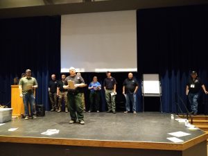 Several people stand side by side on a stage with dark curtains in the background.