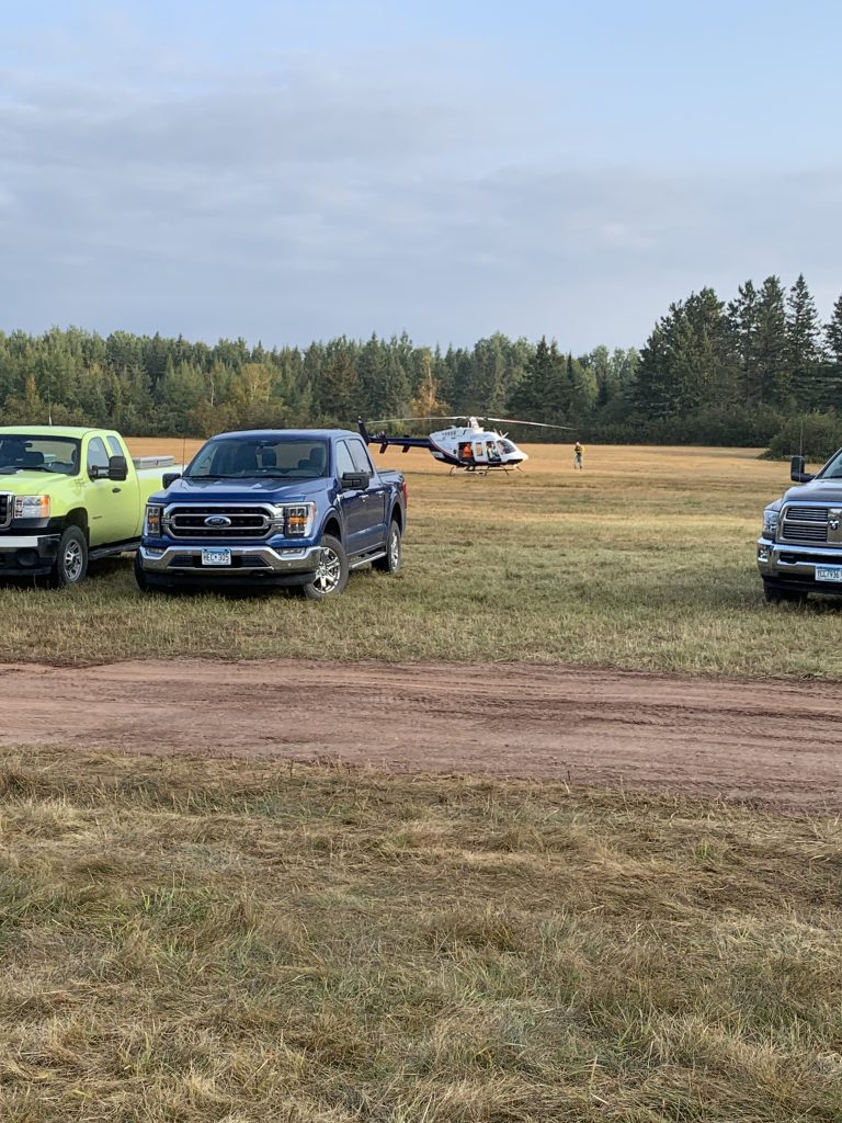 Image of vehicles and a small helicopter parked in a field.