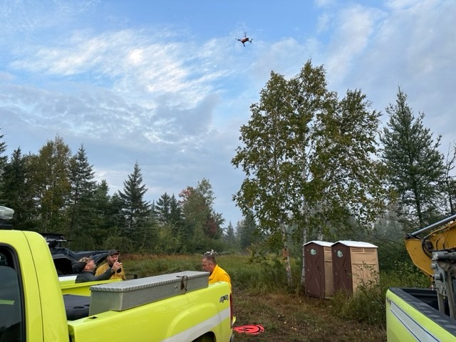 Image of a drone over a group of trees. Porta-pottis and trucks in the photo as well. 