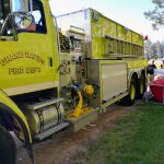 A large yellow fire engine fills up a red portable tank with water.