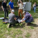 Five people work to construct an outdoor weather station.