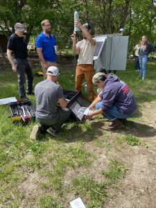 Five people work to construct an outdoor weather station.