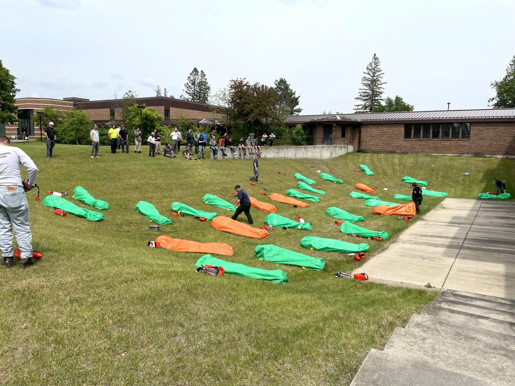 Wildfire Academy students on grass laying inside deployed fire shelters